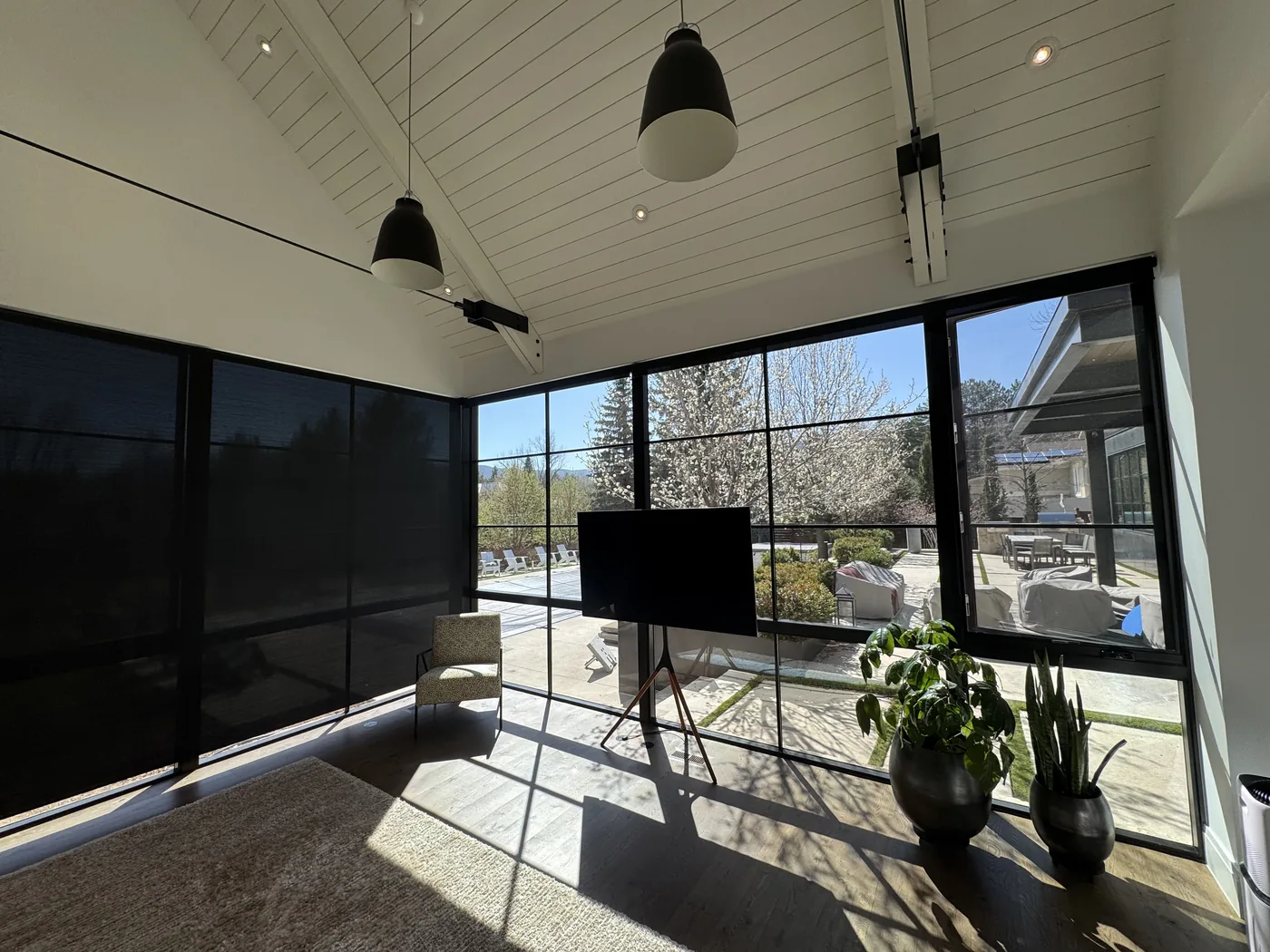 Dark solar roller shades installed on floor-to-ceiling black steel frame windows in a Boulder sunroom, motorized window coverings by Howard's Draperies